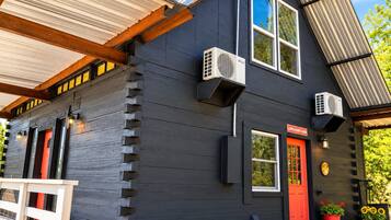 A log cabin with a red door, air conditioning units, and a welcome sign.