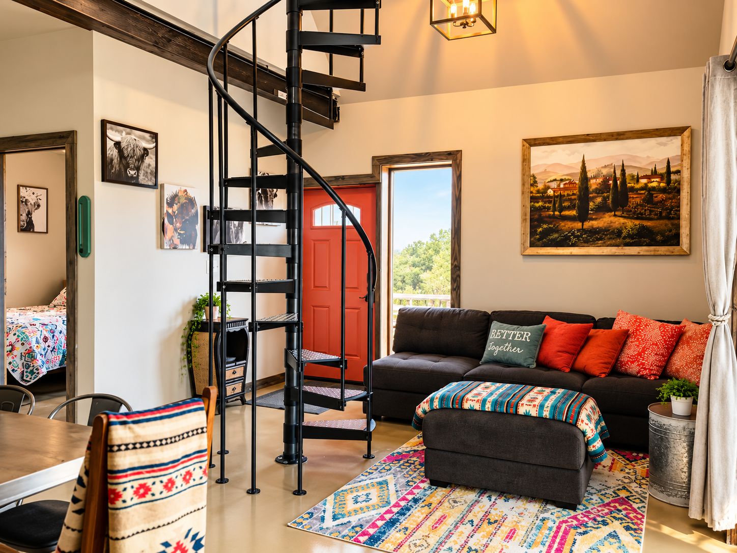 A modern living room with a black spiral staircase, a red door, a black sofa with colorful cushions, and a large landscape painting on the wall.
