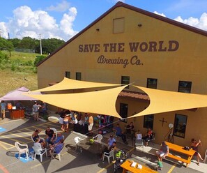En byggnad med skylten ”SAVE THE WORLD Brewing Co.” och ett utomhusområde med sittplatser där folk sitter.
