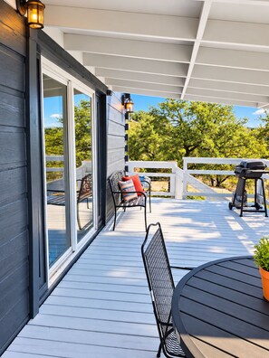 Eine überdachte Terrasse im Freien mit Grill, Tisch und Stühlen.