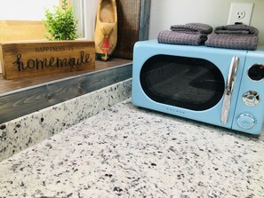 Une cuisine avec un micro-ondes bleu, un panneau en bois sur lequel est écrit « Le bonheur, c’est fait maison », et une plante.