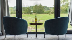 Una habitación con dos sillas azules mirando una mesa redonda pequeña con una botella y dos vasos.