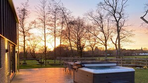 Un patio con jacuzzi, mobiliario exterior y vistas a árboles y un atardecer.