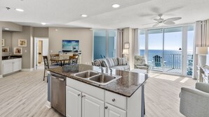 Amplia sala de estar con cocina, comedor y balcón con vista al océano.