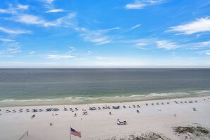Uma praia com guarda-sóis e cadeiras de praia, uma bandeira e vista do oceano.