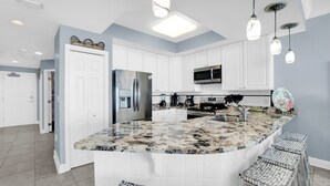 A modern kitchen with white cabinets, a granite island, stainless steel appliances, and pendant lighting. - San Carlos 1407 by Liquid Life (Gulf Shores)