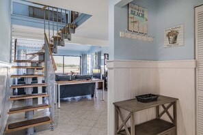A spacious living area with a staircase leading to an upper level, a cozy seating area with a sofa and coffee table, and a wall with decorative signs. - Marsh Haven - Beautiful marsh view, center island, walk to the beach, 236 Tennis Villa (Fripp Island)