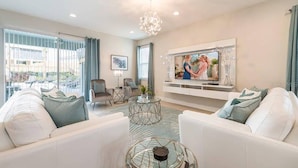 A modern living room with a sofa set, a glass coffee table, and a television mounted on the wall. - Encore Resort 11 Bedroom Home with Pool (2117) (Kissimmee)