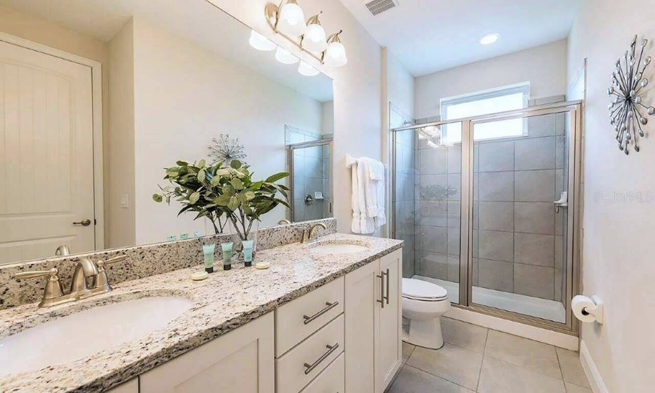 Une salle de bain avec un comptoir en granit, un lavabo, un miroir, un espace douche et des toilettes.