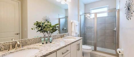 Une salle de bain avec un comptoir en granit, un lavabo, un miroir, un espace douche et des toilettes.