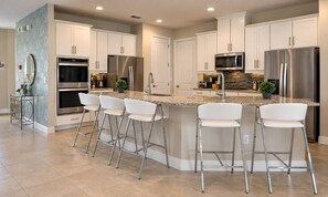 A modern kitchen with white cabinetry, stainless steel appliances, and a central island with bar stools. - Encore Resort 11 Bedroom Home with Pool (2117) (Kissimmee)
