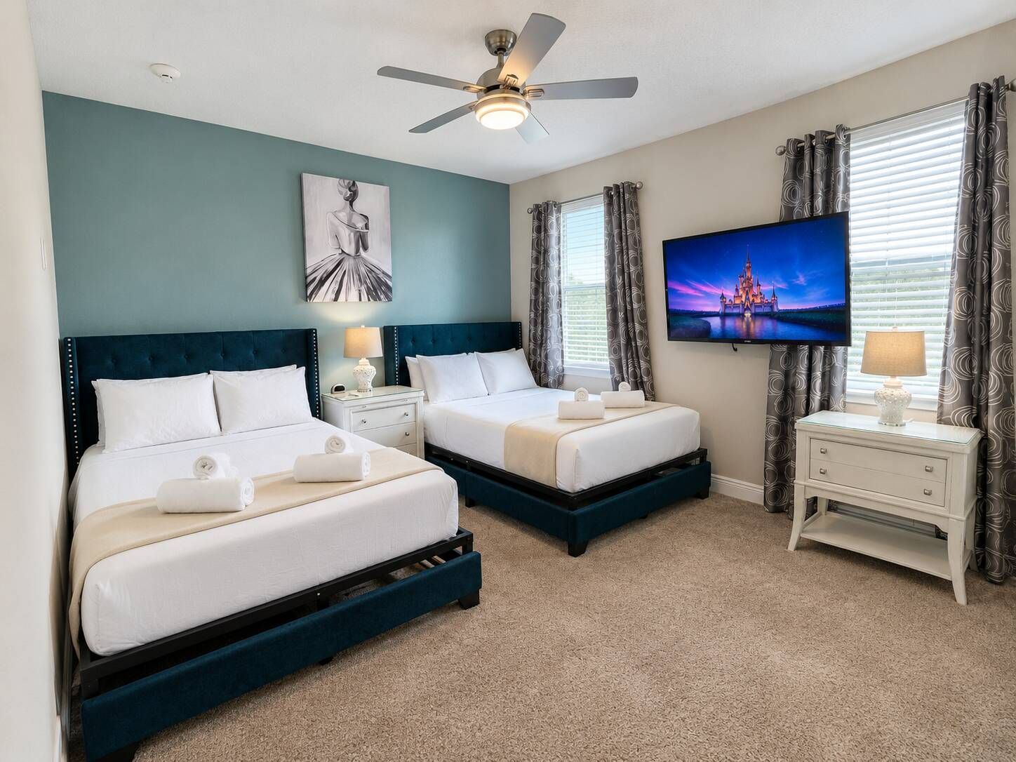 A hotel room with two beds, a ceiling fan, a flat-screen TV, and a painting on the wall.