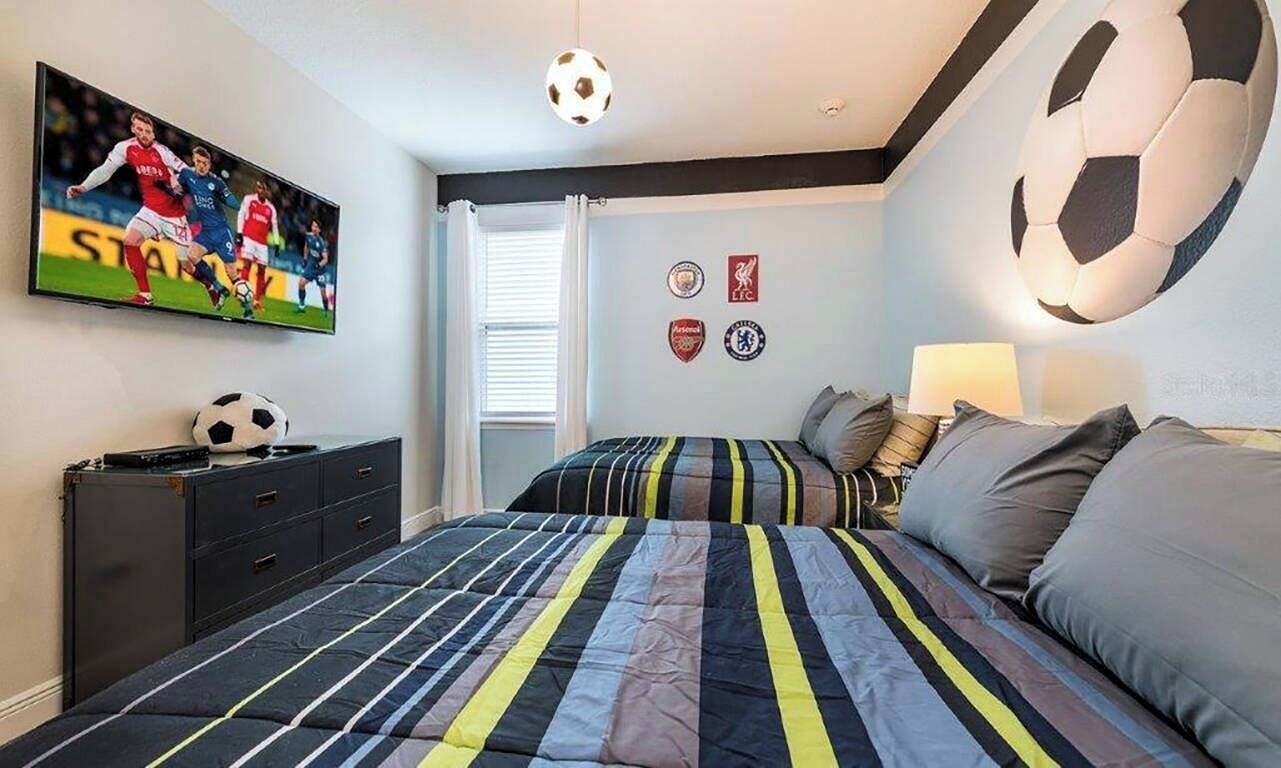 Une chambre à coucher avec un lit, une télévision, un ballon de foot accroché au mur et une étagère sur laquelle se trouve un autre ballon de foot.