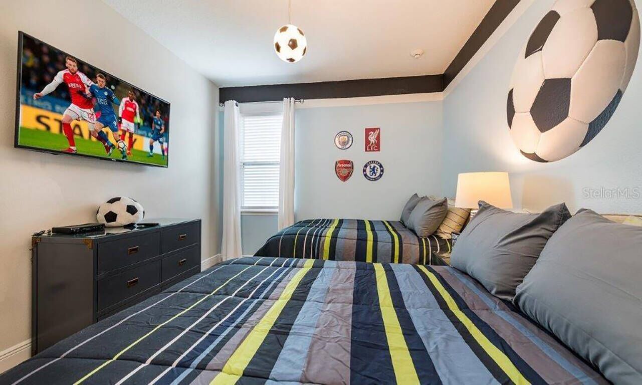 Een slaapkamer met een bed, een televisie, een voetballposter en sportteam badges.