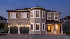 A two-story house with a garage, a covered porch, and a landscaped front yard. - Encore Resort 11 Bedroom Home with Pool (2117) (Kissimmee)