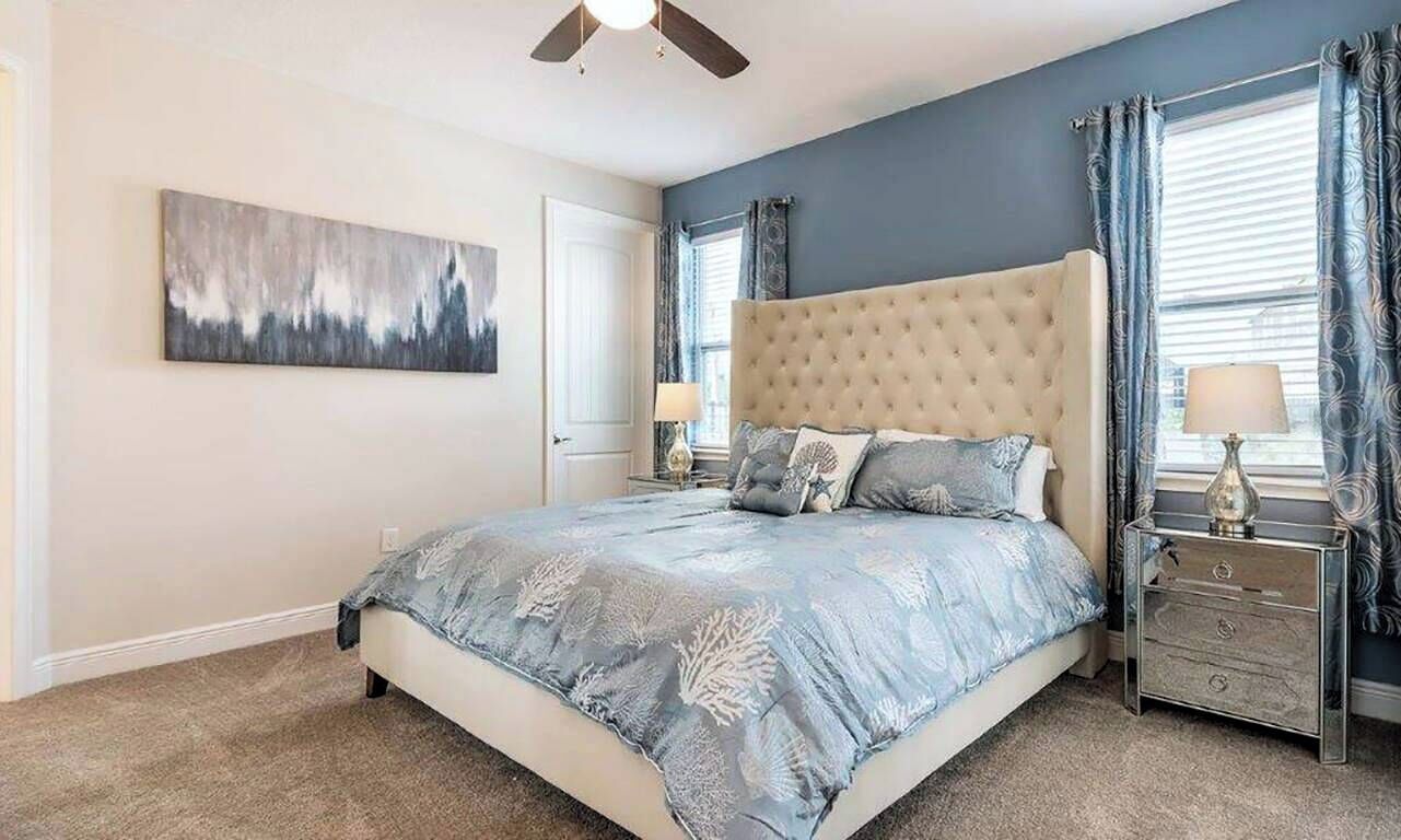 Ein Schlafzimmer mit einem großen Bett, einem Deckenventilator, einem Nachttisch mit Lampe und einem Fenster mit Vorhängen.