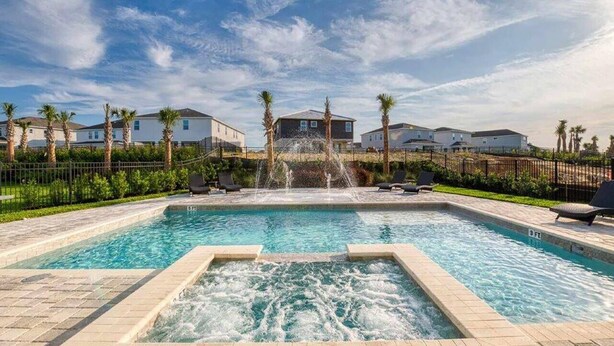 A rectangular pool with a central water feature, surrounded by a paved deck and palm trees. - Encore Resort 11 Bedroom Home with Pool (2117) (Kissimmee)