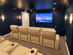 A home theater room with a large flat-screen TV, reclining leather chairs, and a dark blue wall. - Encore Resort 11 Bedroom Home with Pool (2117) (Kissimmee)