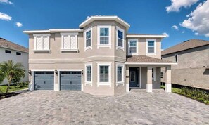 A two-story residential building with a garage, a covered entryway, and a landscaped driveway. - Encore Resort 11 Bedroom Home with Pool (2117) (Kissimmee)
