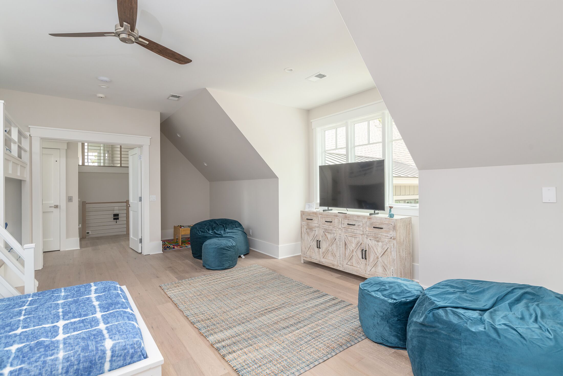 Ein geräumiges Wohnzimmer mit hoher Decke, Deckenventilator, großem Fernseher und Holzschrank.