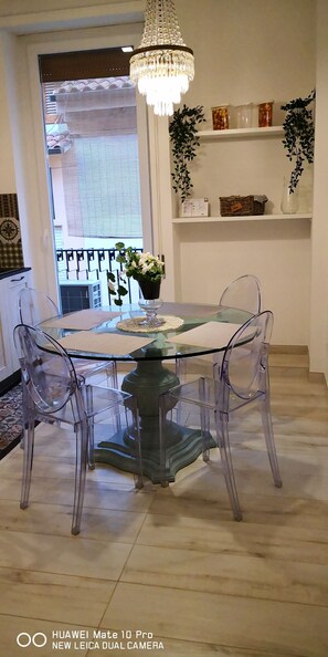 A dining area with a glass table and chairs, a chandelier, and a view of the outside balcony.