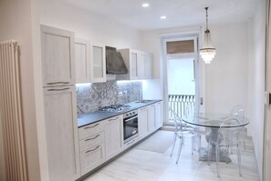 A modern kitchen with white cabinets, a gas stove, and a glass dining table with chairs.