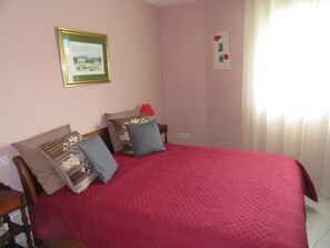 A bedroom with a large bed, multiple pillows, a bedside table, a lamp, and a framed picture on the wall.