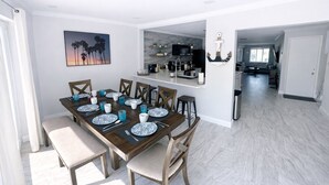 A dining area with a wooden table set for six, a kitchen in the background, and a view of the living area. - Paradise Palms Beach house with HEATED POOL🏖🌅🐬 (Largo)