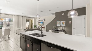 Cozinha moderna com uma ilha grande, eletrodomésticos de aço inoxidável, iluminação pendente e vista para a sala de estar.