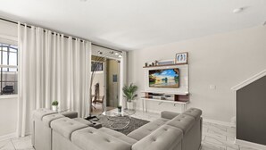 Uma sala de estar moderna com um sofá seccional, uma TV de tela plana e uma mesa de centro de vidro.