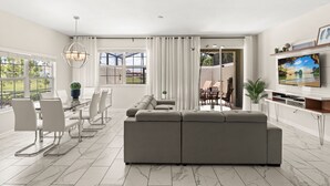 Uma sala de estar moderna com um sofá modular, mesa de jantar, cadeiras e uma televisão.