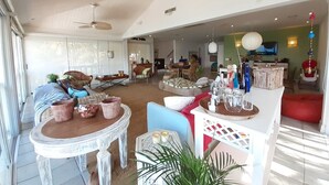 Un salón espacioso con una mesa de comedor, sillas y un sofá. Hay ventiladores de techo, un televisor y varios objetos decorativos.