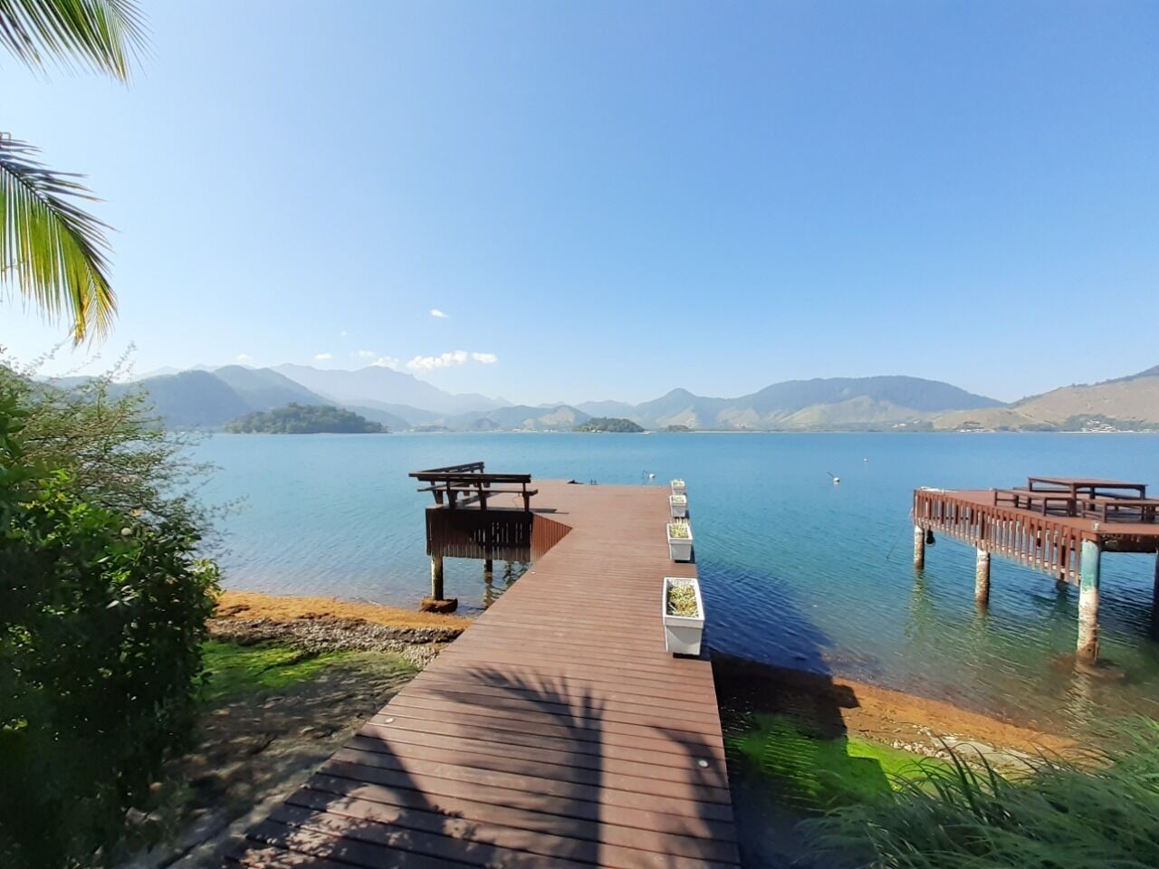 Ein hölzerner Steg erstreckt sich über einen ruhigen See, im Hintergrund sind Berge zu sehen.