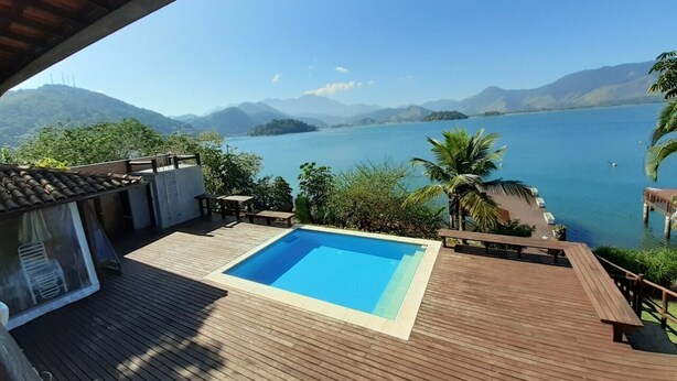 Una terraza de madera con piscina y vistas a un lago y montañas.