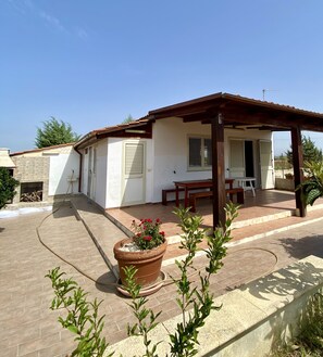 A house with a covered patio, a stone fireplace, and a garden with potted plants.