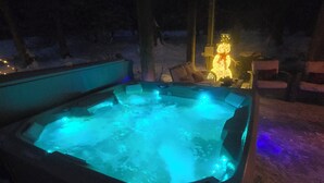 A hot tub with blue lighting, surrounded by outdoor seating and a snow-covered ground.