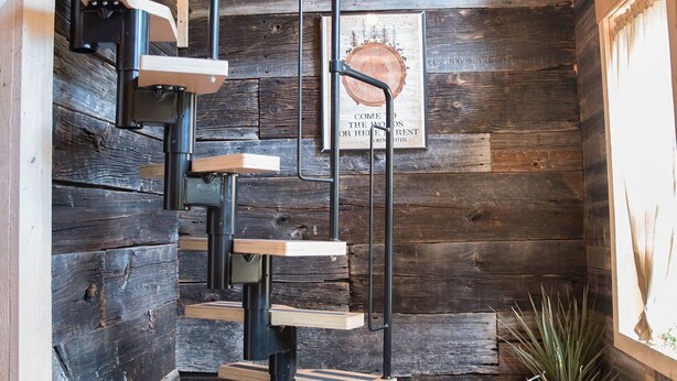 A wooden interior with a spiral staircase, a framed artwork on the wall, and a potted plant.