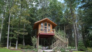 A wooden cabin with a balcony, surrounded by a forest.