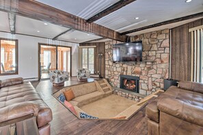 A spacious living room with a stone fireplace, leather sofas, and a large TV mounted on the wall.