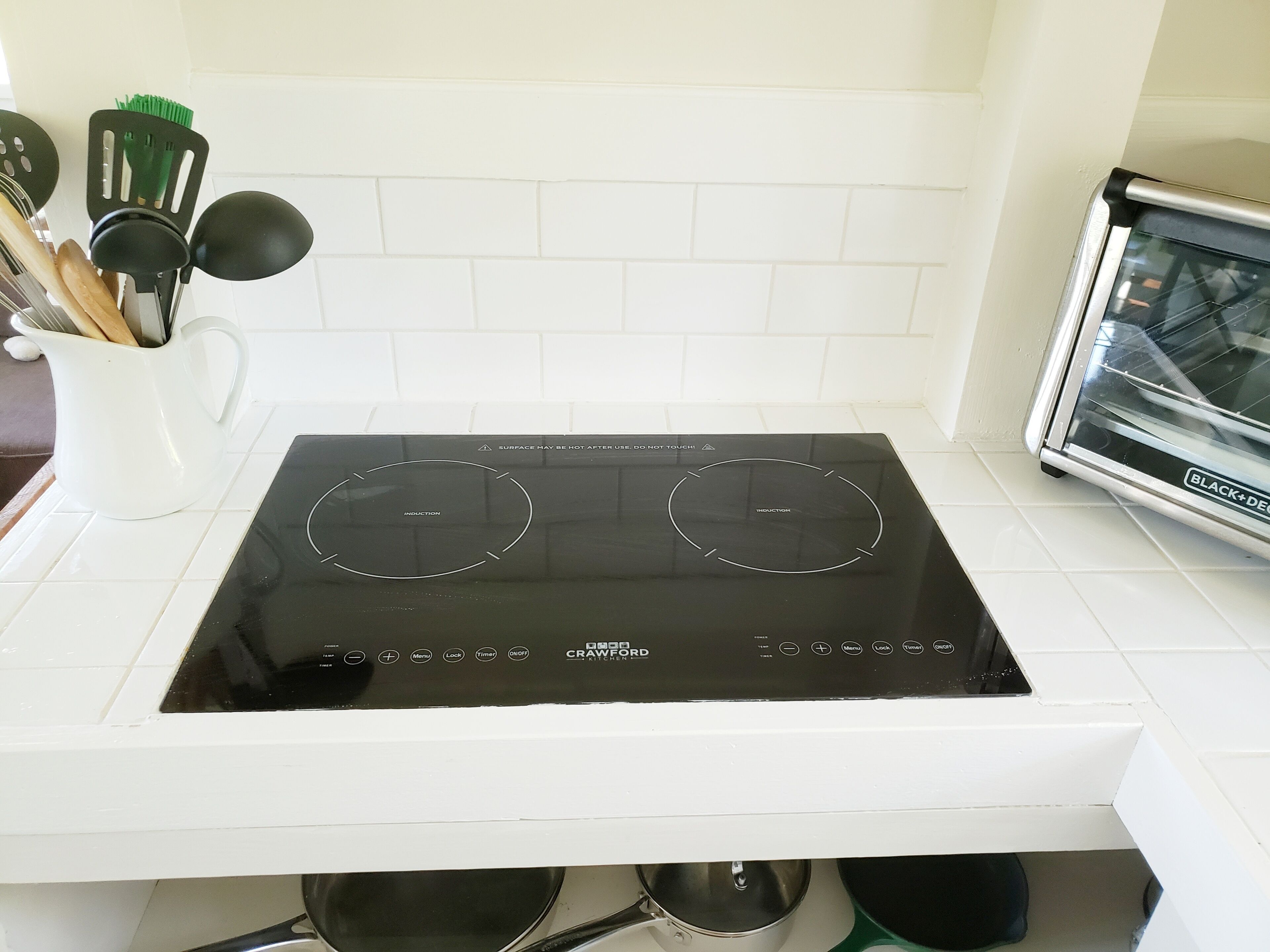 Una cucina con piano cottura a induzione nero, schienale bianco e forno tostatutto.