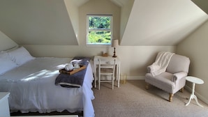 Ein Schlafzimmer mit Bett, einem Sessel, einem kleinen Tisch, einem Fenster mit Blick auf Grünflächen und einer Deckenleuchte.
