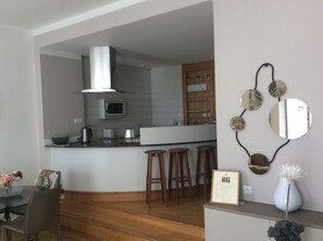 A modern kitchen with a central island, wooden stools, a white vase with a flower, and a framed certificate on a counter.