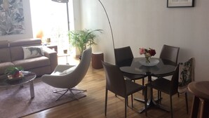 Ett modernt vardagsrum med en soffa, ett runt matbord med stolar, en golvlampa och en krukväxt.