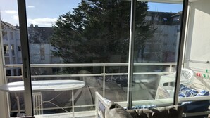 Un balcon doté d’une rambarde en verre, une table blanche et un canapé avec des coussins.