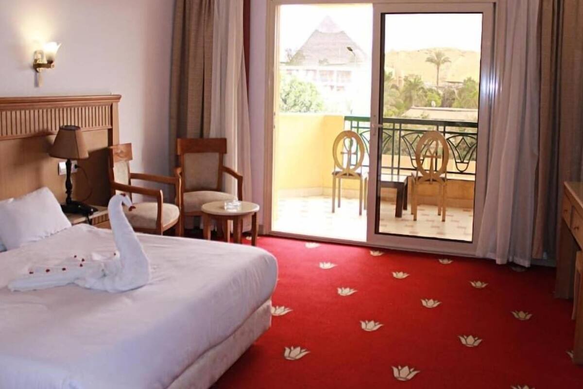 A hotel room with a bed, a chair, a small table, a lamp, and a balcony with chairs.