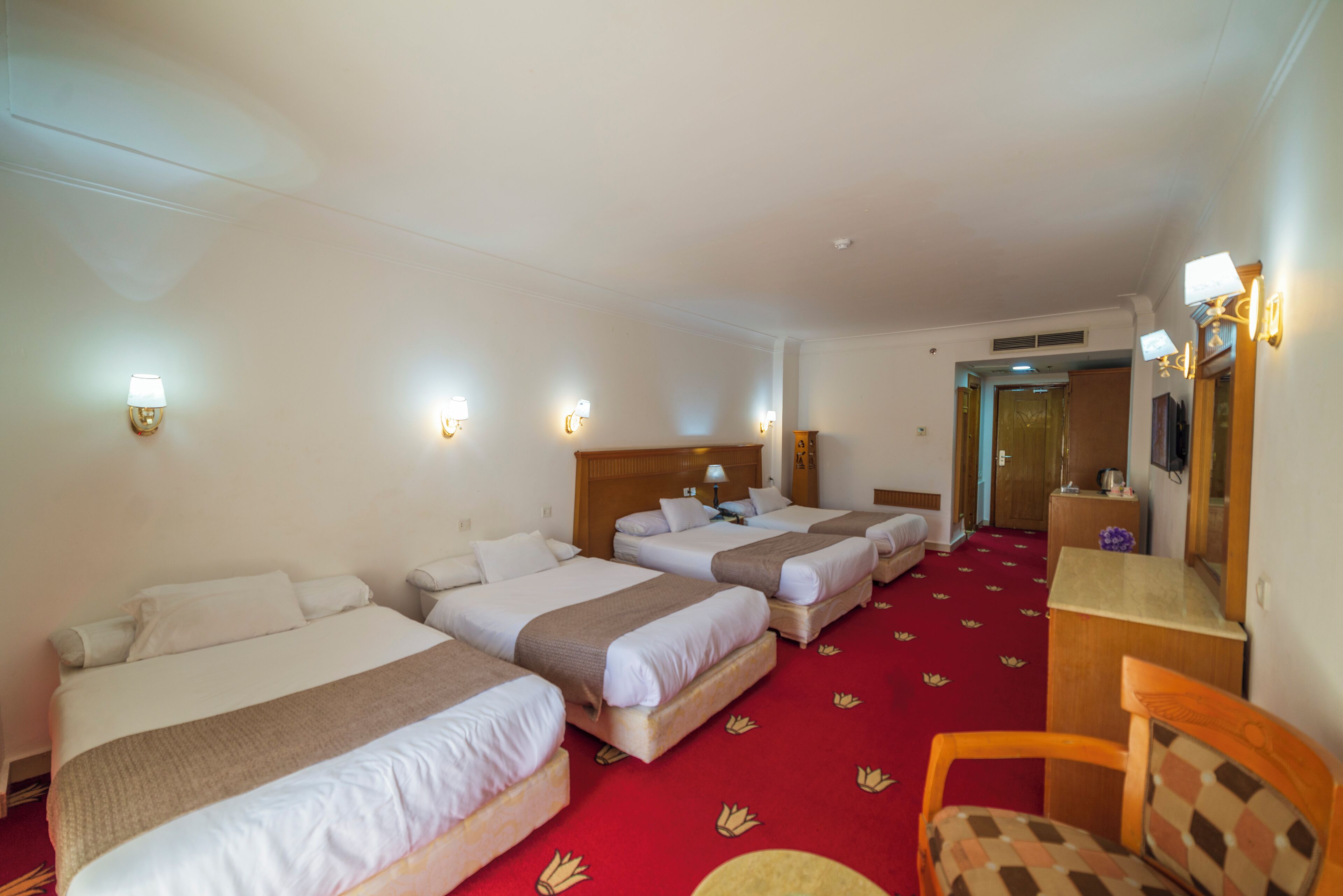 A hotel room with three beds, a desk, and a chair.