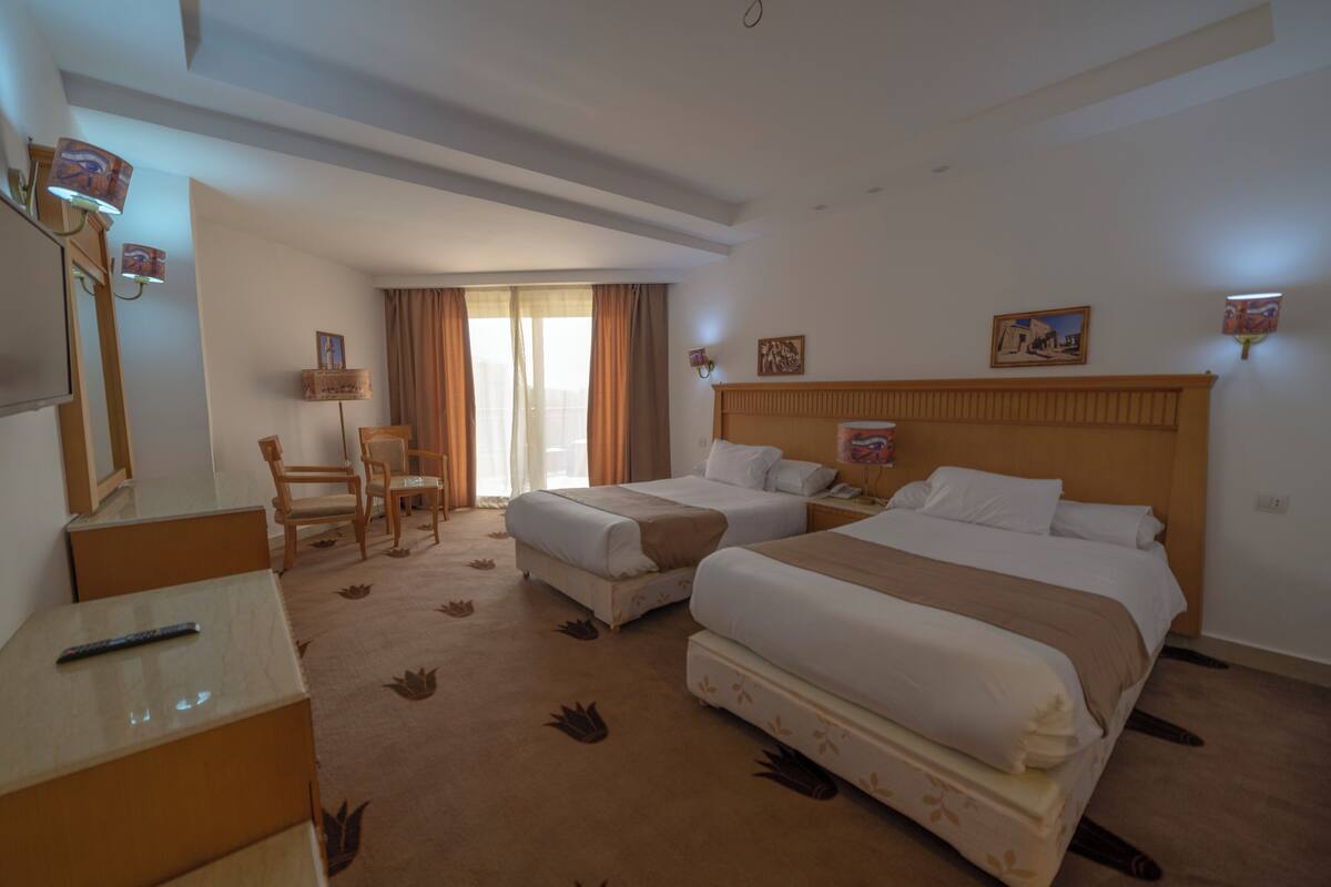 A hotel room with two beds, a desk, a chair, and a large window with curtains.