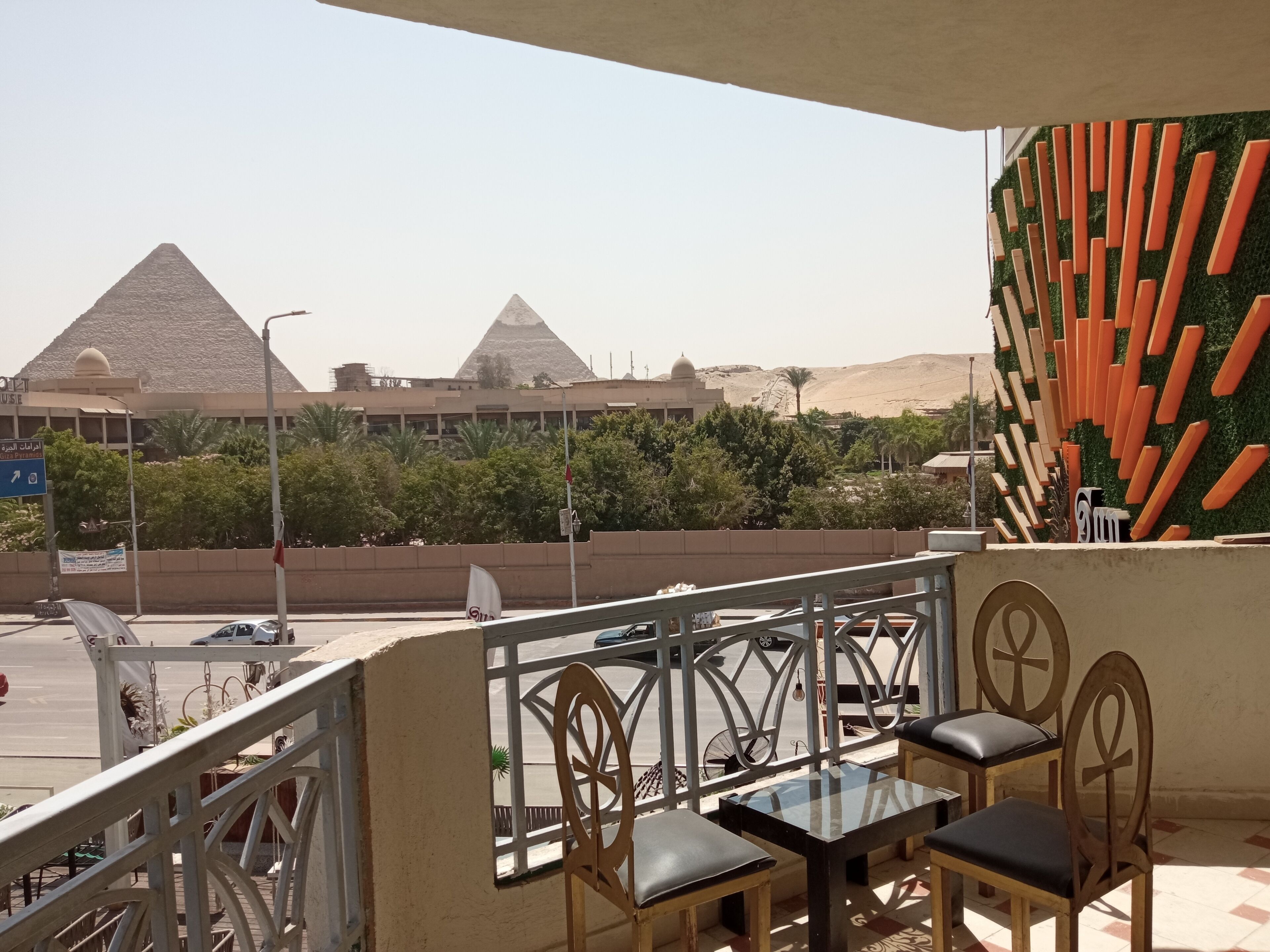 Un balcon avec vue sur les pyramides, un mur végétal avec des lattes de bois, et une table avec des chaises.