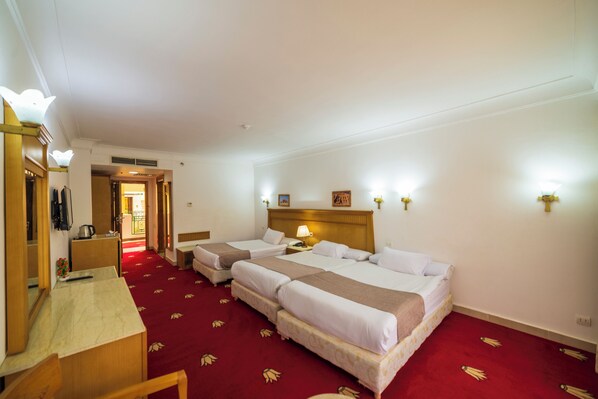 A hotel room with two beds, a desk, and a red carpet.