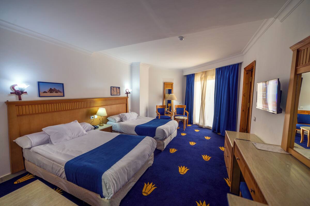 A hotel room with two beds, a desk, a chair, a lamp, and a television.